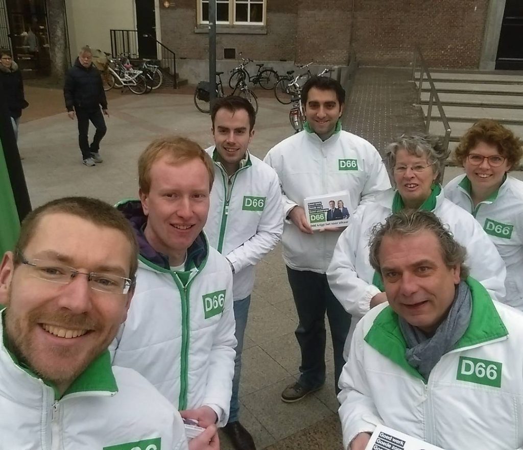 Straatcampagne van D66: zeven mensen met een witte jas met D66-logo kijken in de camera.